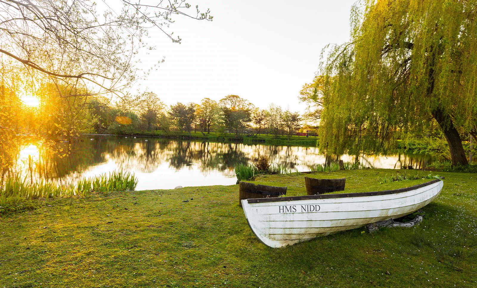 HMS Nidd rests on the ground beside the lake, bathed in the golden glow of sunset - a peaceful, picturesque spot to discover on your adventures.