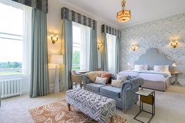 Spacious manor house bedroom at Heythrop Park featuring a bed, chair, lamp, and a large window for natural light.