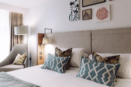 A deluxe bedroom at Heythrop Park featuring a cozy bed, elegant chair, and a bright window.