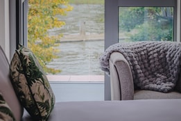View of the River Thames from a bedroom inside The Runnymede on Thames Hotel, with a bed and soft chair in the foreground