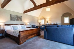 Royal bedroom with a king-size bed, separate lounge seating area, and exposed wooden beams.