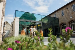 Modern glass-fronted hotel atrium entrance surrounded by landscaped gardens.