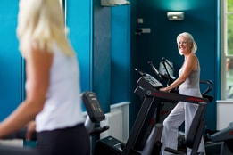Two people in the gym at Holme Lacy House, smiling at each other as they work out