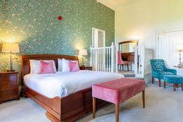 Spacious hotel bedroom with botanical wallpaper, king-size bed and elegant seating area.
