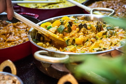 A chef stirring a chickpea curry made for the market kitchen, surrounded by other curries