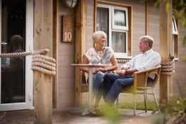 Two couples relax on the patio of a bay cottage, seated outdoors near the water and enjoying a peaceful coastal atmosphere.