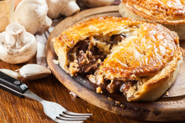 Close up of a beef and mushroom pie that has been opened with a fork, releasing delicious flavoursome gravy