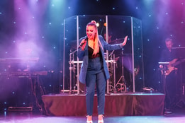 A woman in a blue suit performing on stage at Cricket St Thomas