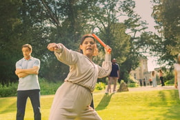 Angie stands firm with an axe ready to throw at the target, Mick looks on in the background with slight concern