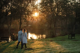 Two people walking hand in hand by a lake at sunset