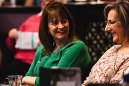 Two women at a table, smiling and enjoying each other's company during a BBC History Magazine weekend event.
