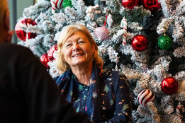 A woman smiling in festive dress in front of a christmas tree