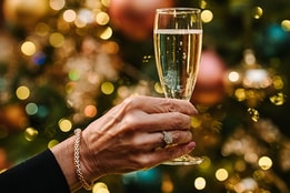 Close up of a glass of prosecco held in front of a christmas tree