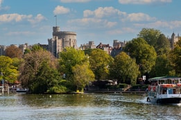 A view of Windsor Castle from the River Thames, featuring a boat in the foreground and surrounded by greenery