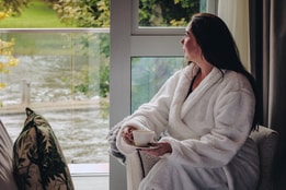 A guest enjoying a cup of tea and the incredible view from her balcony inside a double deluxe room at The Runnymede on Thames