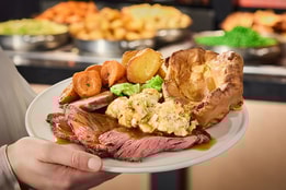 A plate full of roast dinner delights held by someone in front of the carvery selection