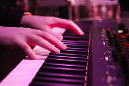 Close up of a person's hands as they play the piano, with a purple hue from the lighting