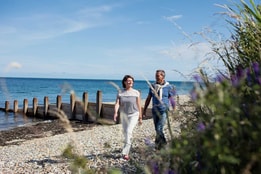 A man and woman stroll together along a serene beach, enjoying the sun and waves.