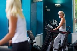 Two people in the gym at Holme Lacy House, smiling at each other as they work out