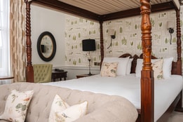 Historic bedroom with a carved four-poster bed, botanical wallpaper and upholstered seating.