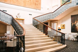 Grand hotel staircase with sweeping balustrades, artwork and elegant lounge seating.