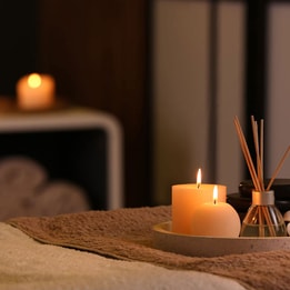Spa treatment room with lit candles, diffuser reeds and towels creating a calming atmosphere