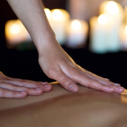 Therapists hands giving a back massage with candles in the background
