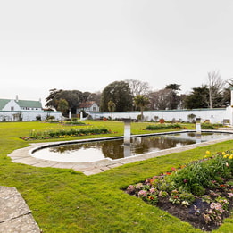 A serene garden featuring a tranquil pond and an elegant fountain, surrounded by lush greenery and vibrant flowers.