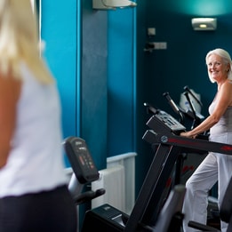 Two people in the gym at Holme Lacy House, smiling at each other as they work out