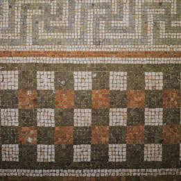 Close-up of an intricate geometric mosaic floor featuring repeating patterns in cream, grey, black and terracotta-coloured tiles.
