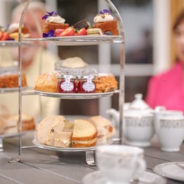 A tiered stand filled with assorted pastries, scones, and jams, accompanied by fine china teacups and teapots on a rustic table.