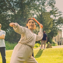 Angie stands firm with an axe ready to throw at the target, Mick looks on in the background with slight concern