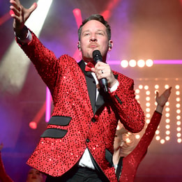 Singer in red suit and black bow tie performing Cirque: The Greatest Show on stage at Warner Hotels.