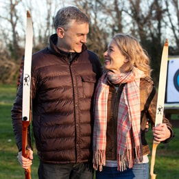 A couple gazing into each others eyes as they hold bows during a game of archery