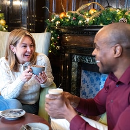 Two guests smiling at each other with hot drinks in hand