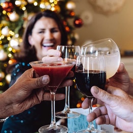 Group of people raising wine glasses in front of a beautifully decorated Christmas tree.