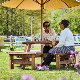 Two guests sat on a bench with an umbrella in the sunshine with sunglasses