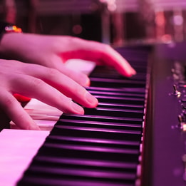 Close up of a person's hands as they play the piano, with a purple hue from the lighting
