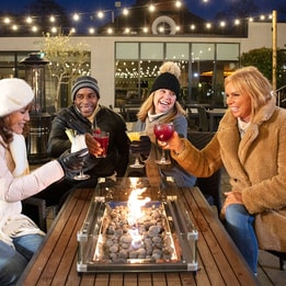 Four friends joyfully toasting drinks over a festive fire pit, creating a warm and inviting atmosphere.