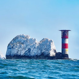 The Needles Lighthouse standing beside the iconic white chalk stacks off the coast of the Isle of Wight.