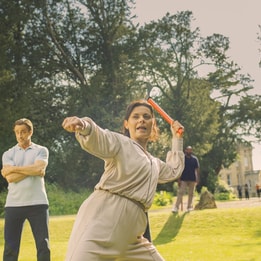 Angie prepares to throw an axe and Mick looks on nervously in the background seeing her pent up rage