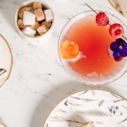 Aerial shot of a marble table with a cocktail, cup of tea and pot of sugar cubes in view