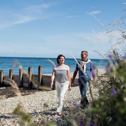 A man and woman stroll together along a serene beach, enjoying the sun and waves.