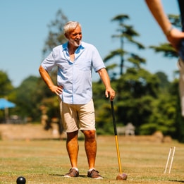 Two people enjoy a relaxed game of croquet on a sunny lawn, mallets in hand and wickets set across the grass.