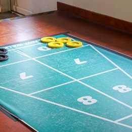 A green and black shuffleboard game board set up for play at Norton Grange, featuring smooth lanes and scoring areas.