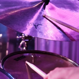Close-up of a drum kit cymbal and drumsticks under stage lighting.
