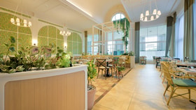 The front area of the Market Kitchen at Heythrop Park, with green walls, plants and dining tables and chairs