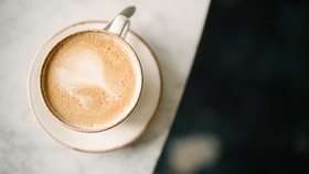Overhead view of a creamy coffee in a ceramic cup on a saucer, placed on a light marble table.