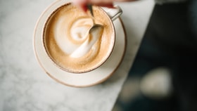 Overhead view of a cup of frothy coffee as a spoon stirs the foam, creating a swirl pattern.