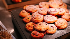 Selection of golden, spiral pastries dusted with icing sugar and studded with raisins, arranged on a dark serving tray.